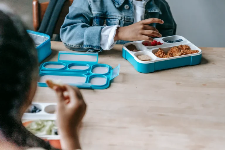 Jersey politician calls for more food funding as free fruit scheme ends Crop faceless classmates sitting at table with lunch boxes with various food and eating during break